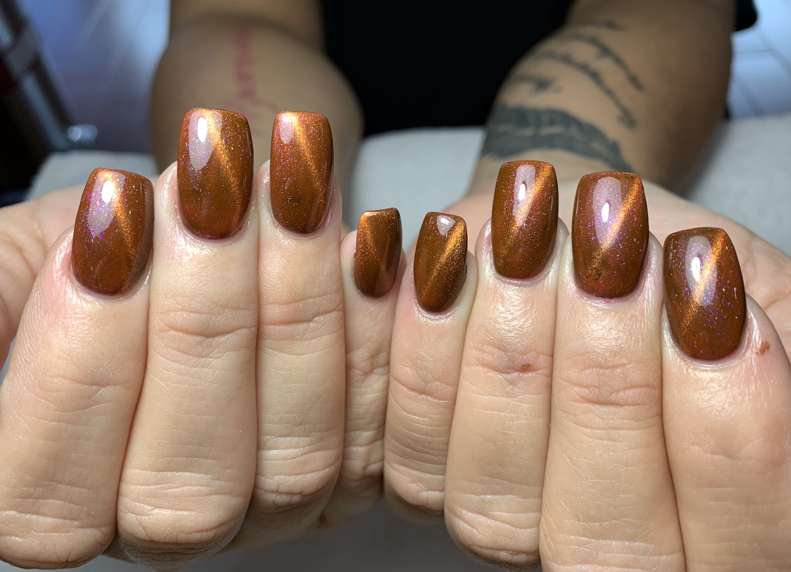 Two hands with glossy copper cat-eye nails catching the light.
