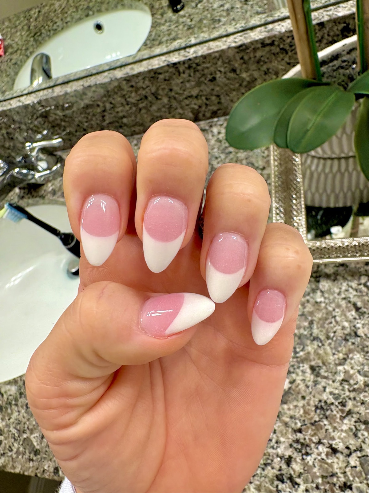 A hand with almond nails in a soft pink French manicure with glossy white tips.